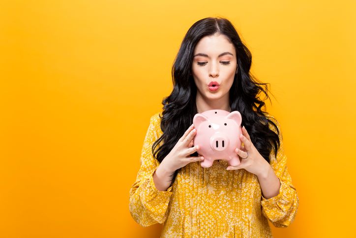 Finansijski horoskop za leto 2024; prelepa crnokosa devojka drži ružičastu kasicu prasicu, na žutoj pozadini